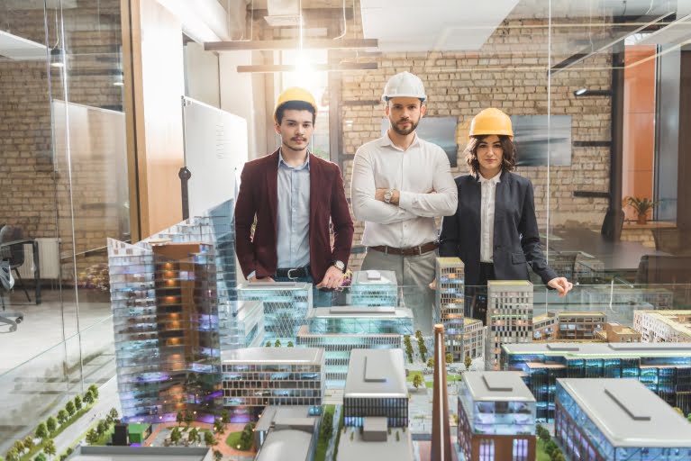 team of architects in hard hats in front of miniature town model at office